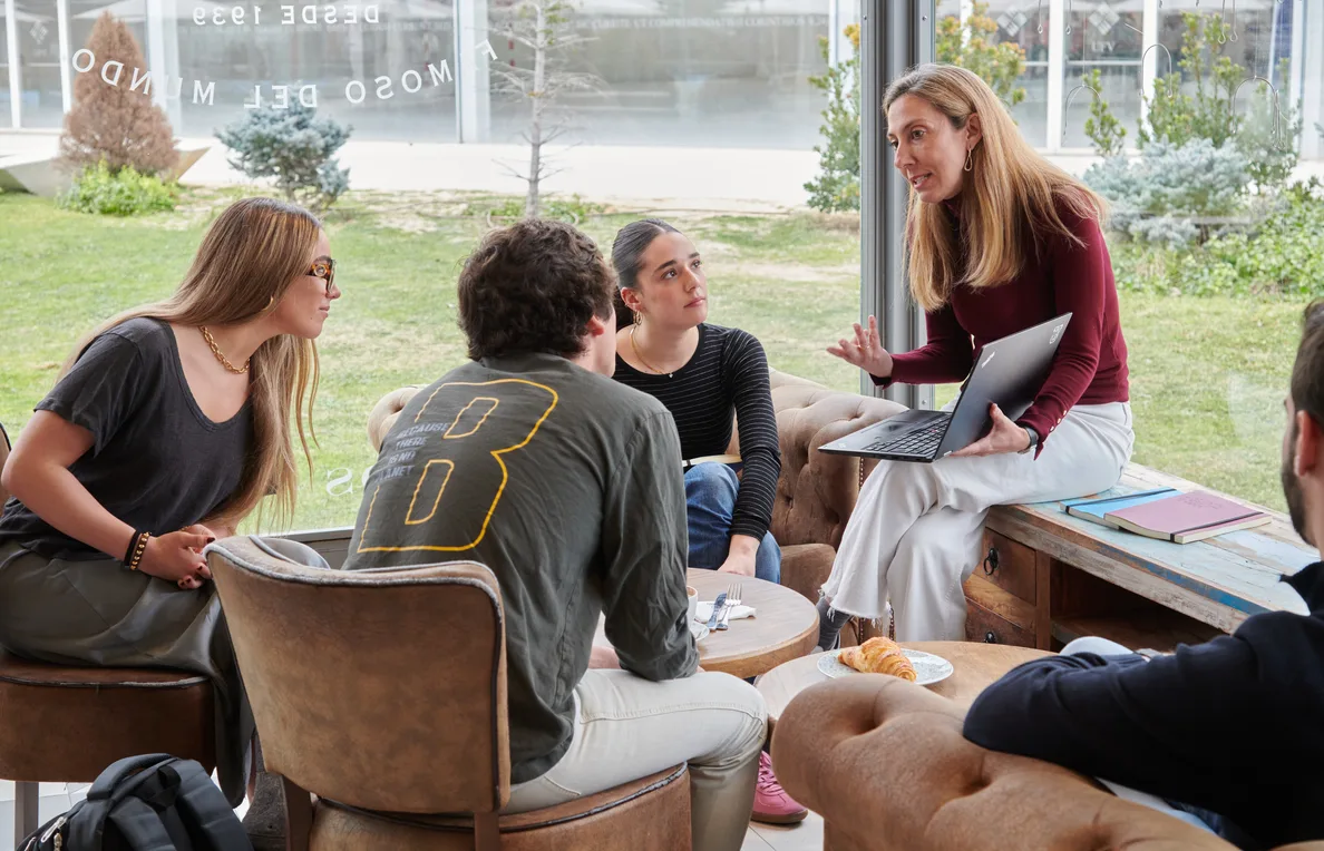 Una profesora conversa con varios estudiantes sentados en una zona común del campus