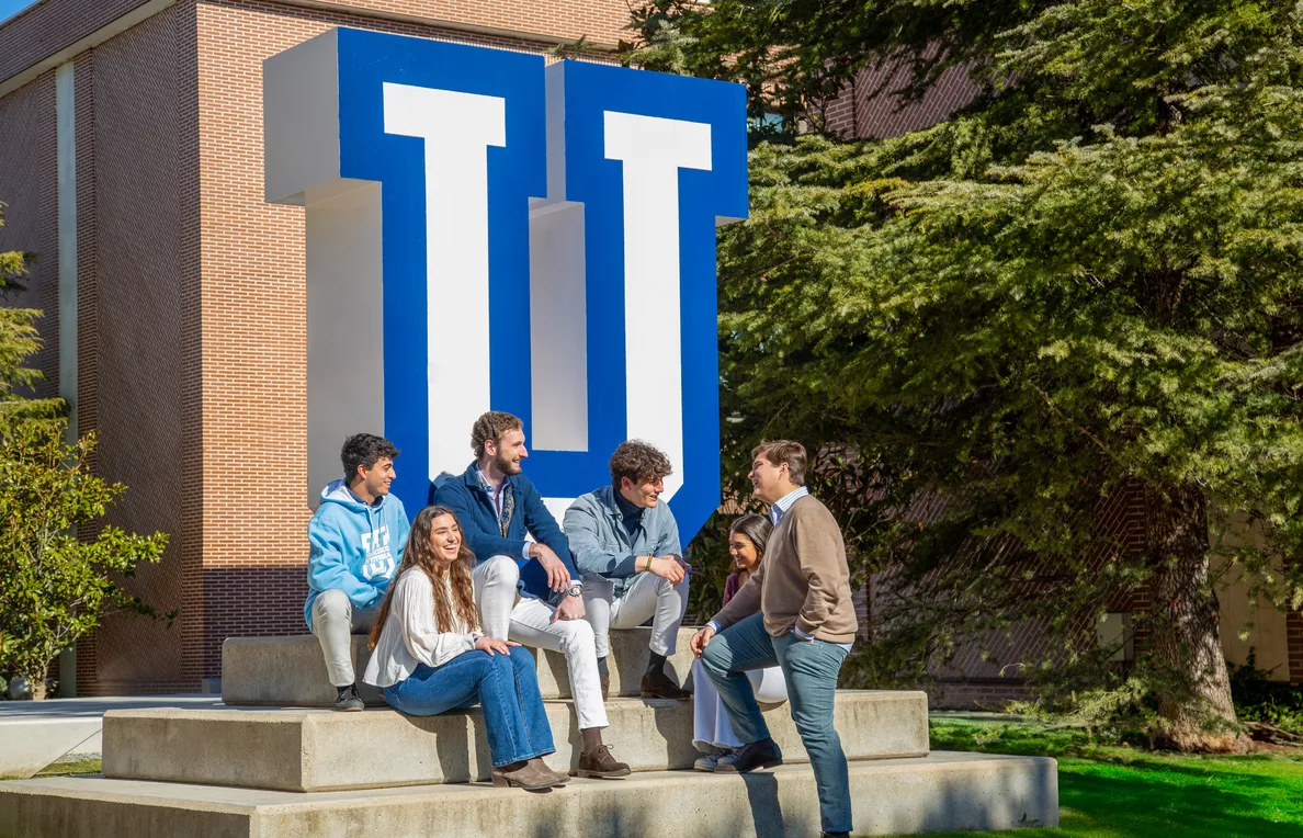 Un grupo de estudiantes charla sentado junto a la gran letra U del campus